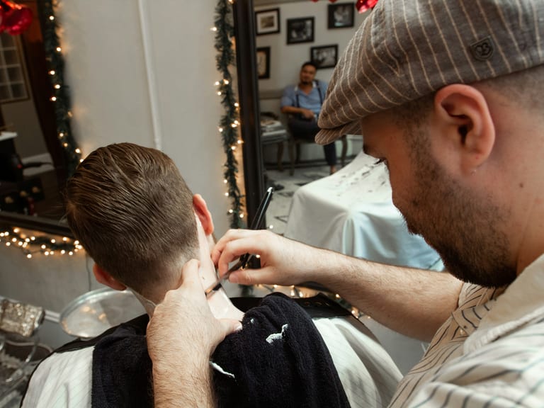 A barber trimming a young client’s neckline in a warm-lit shop